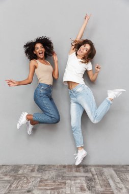 Tam uzunlukta birlikte atlama ve gri arka plan üzerinde izole kutlama iki neşeli genç kadın portresi