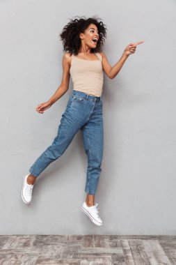 Tam uzunlukta atlama ve parmakla kopya alanı, gri arka plan üzerinde mutlu bir genç Afrikalı kadın portresi