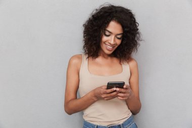 Cep telefonunuzun ve gri arka plan üzerinde gülümseyen genç Afrikalı kadın portresi