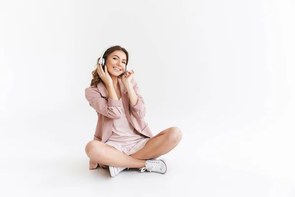 白い壁の背景がヘッドフォンで音楽を聴く上分離された若いかわいい美しい女性のイメージ — ストック写真