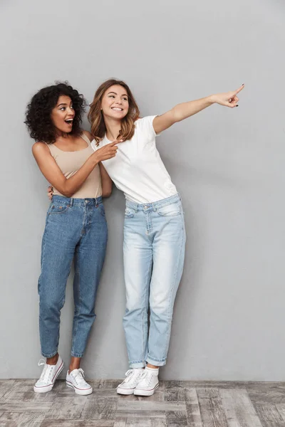 Full Length Portrait Two Cheerful Young Women Standing Together Pointing — Stock Photo, Image