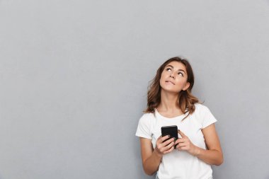 Cep telefonu tutan ve gri arka plan üzerinde de kopya alanı ararken dalgın bir genç kadın portresi