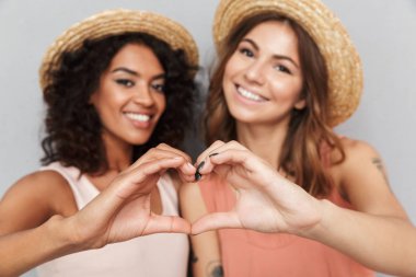 İki genç kadın kollarıyla gri arka plan üzerinde izole kalp jest gösterilen yaz elbise giymiş mutlu portre kadar kapatın