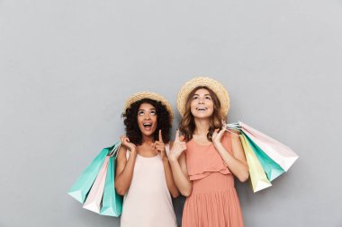 İki mutlu genç kadın portresi alışveriş torbaları tutarak ve gri arka plan üzerinde izole kopya alanı işaret yaz elbise giymiş