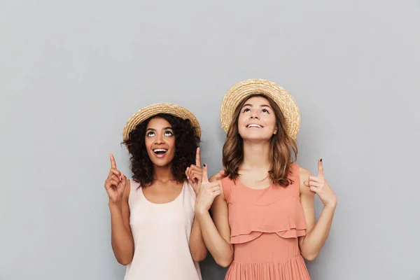 两个快乐的多民族妇女 白种和非洲裔美国女孩的肖像戴草帽微笑着 而手指向上在灰色背景 Copyspace — 图库照片