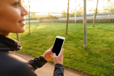 Genç spor kadının açık havada cep telefonuyla fotoğrafını kırpılmış.