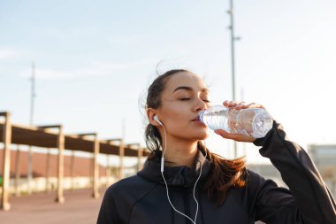 Görüntü güzel genç Asyalı kadın dinleme müzik ile kulaklık içme suyu açık havada spor.