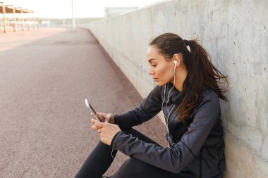 Görüntü ciddi Genç Asyalı açık havada dinleme müzik cep telefonuyla oturan kadın spor.