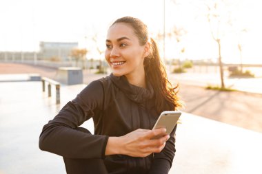Açık havada cep telefonu kullanan neşeli Asyalı genç bir kadının fotoğrafı..