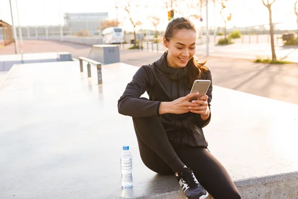 Zdjęcie Wesołej Młodej Azjatyckiej Kobiety Sportowej Siedzącej Zewnątrz Pomocą Telefonu — Zdjęcie stockowe