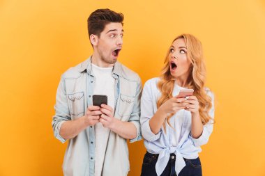 Şaşırmış adam ve birbirine ile açık mouthes bakarak ve akıllı telefonlar üzerinde sarı arka plan izole elinde tutan bir kadın fotoğrafı