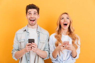 Sarı arka plan üzerinde fotoğraf heyecanlı insanlar erkek ve kadın gülüyor ve yukarı doğru seyir elinde akıllı telefonlar ile izole