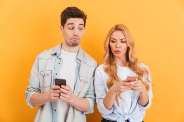 Ciddi adam ve rahat kıyafet birbirlerinin cep telefonları üzerinde sarı arka plan izole bakmak kadın fotoğrafı