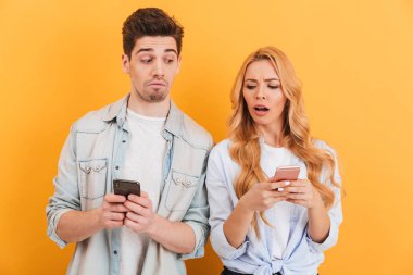 Meraklı adam ve çatık ve birbirlerinin cep telefonları üzerinde sarı arka plan izole bakmak kadın fotoğrafı