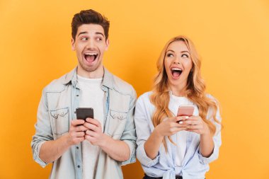 Neşeli erkek ve kadın birbirine bakarak mutlu duyguları ile akıllı telefonlar üzerinde sarı arka plan izole kullanırken fotoğraf