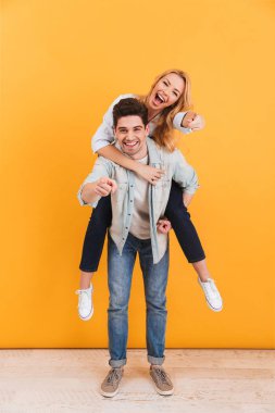 Tam uzunlukta fotoğraf eğleniyor ve sana mutlu kadın sarı arka plan üzerinde izole piggybacking adam suçlamayı gülümseyen çift