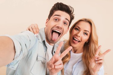 Fotoğraf eğlenceli mutlu çift erkek ve sarılma ve selfie dilini gösteren barış işareti ise sarı arka plan üzerinde izole fotoğrafta kadın