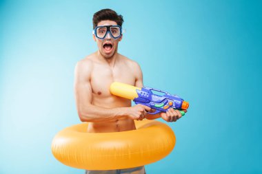 Yüzmek gözlük ve şişme yüzük eğleniyor su silahlar ile mavi arka plan üzerinde neşeli bir genç gömleksiz adam portresi