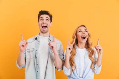 Görüntü içinde casual giyim gülümseyen kadın ve erkek heyecanlı ve yukarı işaret parmağı ile boşaltmak seyir izole sarı arka plan üzerinde