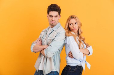 Sarı arka plan üzerinde izole kavga fotoğraf içerledim erkek ve kadın arka arkaya silah ile ayakta denim giysiler katlanmış