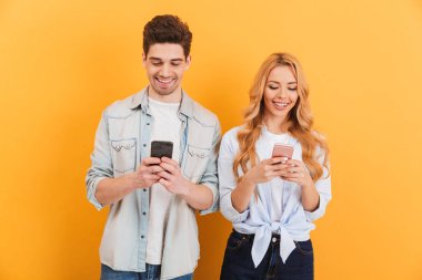 Fotoğraf pozitif kişi adam ve kadın gülümseyen süre cep telefonları üzerinde sarı arka plan izole kullanarak