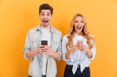 Fotoğraf heyecanlı insanlar erkek ve kadın akıllı telefonlar üzerinde sarı arka plan izole elinde tutarken sevindirici
