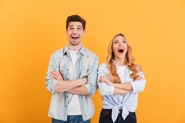 Image of excited people man and woman in basic clothing posing with arms crossed and looking upward isolated over yellow background