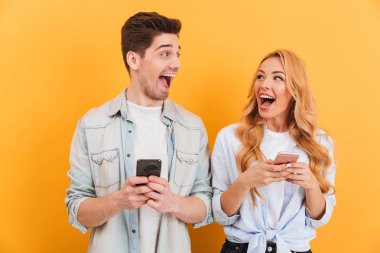Mutlu çift erkek ve birbirine bakarak ve akıllı telefonlar üzerinde sarı arka plan izole elinde tutan bir kadın fotoğrafı