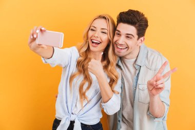 Mutlu çift erkek ve kadın selfie cep telefonu ile izole sarı arka plan üzerinde parmak kameraya el hareketi sırasında fotoğrafta portre