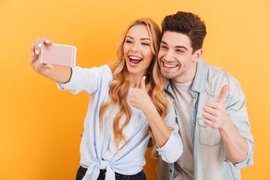 Mutlu çift erkek ve kadın kadar kamera başparmak işaret izole sarı arka plan üzerinde iken selfie cep telefonundan fotoğrafta portre