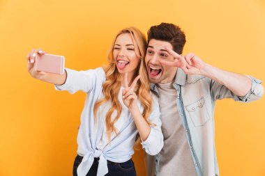 Komik adam ve kadın selfie cep telefonu üzerinde sarı arka plan izole kamera barış sembolleri, el hareketi sırasında fotoğrafta portre