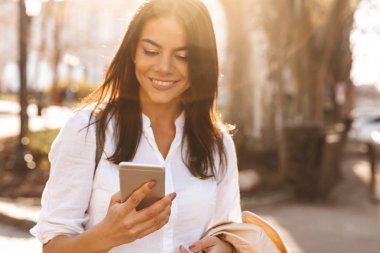 Gülen esmer kadın gömlek onun smartphone açık havada kullanarak görüntü