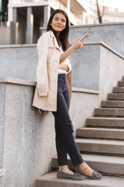 Üzerinde bir merdiven açık havada duran cep telefonu kullanan genç ve güzel kadın