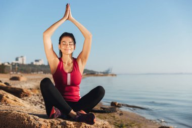 Kumsalda yoga pozisyonda oturan memnun genç sporcumuz