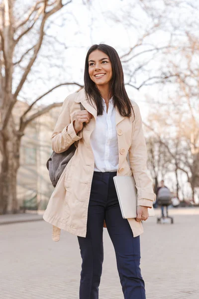 Joven Alegre Vestida Con Abrigo Otoño Llevando Portátil Mientras Camina —  Fotos de Stock