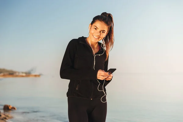 Leende Unga Idrottskvinna Lyssnar Musik Med Hörlurar Och Mobiltelefon När — Stockfoto