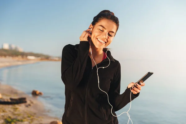 Zadowolony Młody Sprawny Słuchanie Muzyki Przez Słuchawki Telefon Komórkowy Stojąc — Zdjęcie stockowe