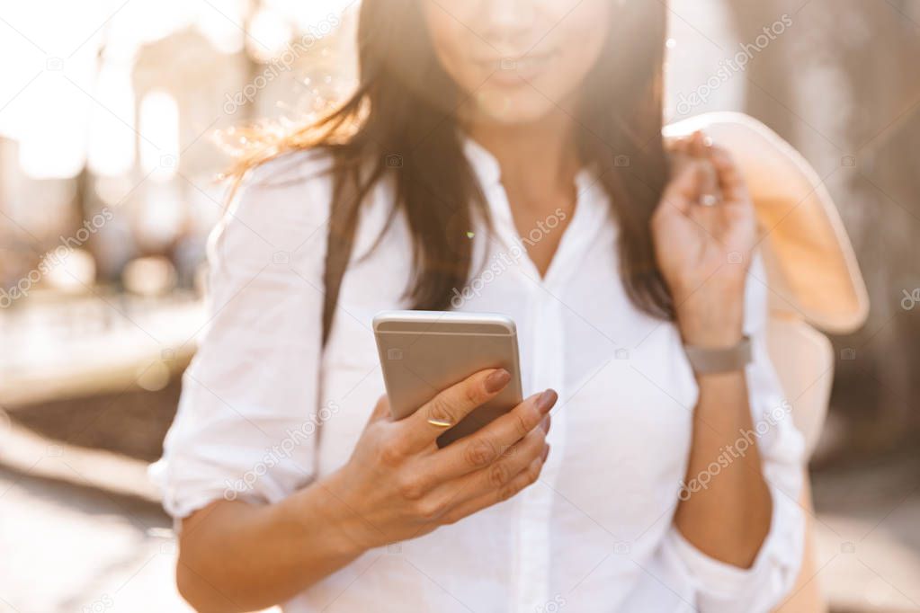 Cropped image of Smiling brunette woman in shirt using smartphone outdoors