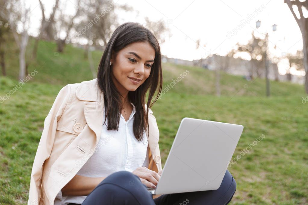 Confident young woman using laptop computer while sitting on a bench outdoors