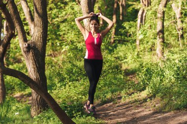 Gülümseyen genç sporcumuz parkta yürüyüş sırasında sırasında germe egzersizleri yapıyor