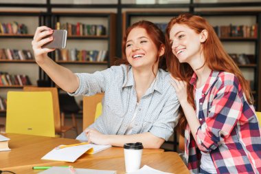 Selfie cep telefonu ile kütüphanede otururken alarak iki mutlu genç kız portresi
