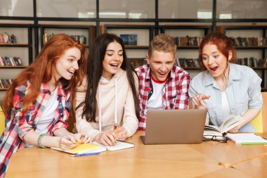 Kütüphanede oturmuş ve dizüstü bilgisayar ekranına bakarak ödev neşeli Genç Grup