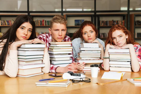 一群疲惫的青少年坐在图书馆桌上 大堆书 — 图库照片