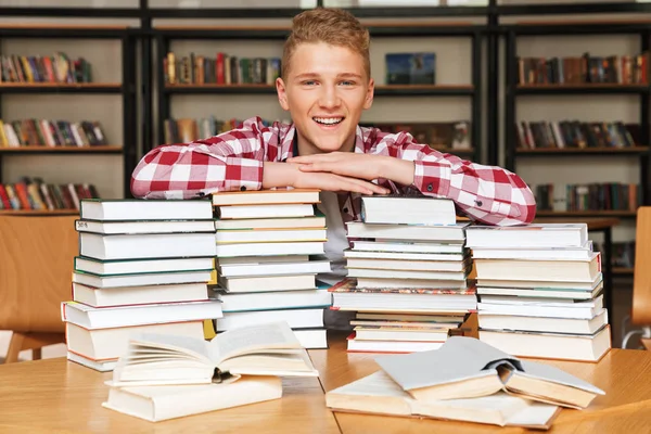 Χαμογελώντας Εφηβικό Αγόρι Που Κάθεται Στο Τραπέζι Βιβλιοθήκη Μεγάλες Στοίβες — Φωτογραφία Αρχείου