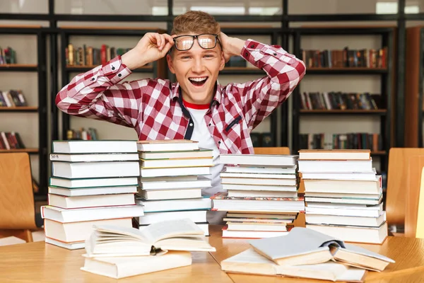 Jovem Alegre Sentado Mesa Biblioteca Com Grandes Pilhas Livros — Fotografia de Stock