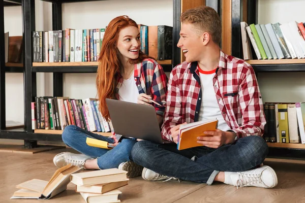 Wesoły Para Nastoletnich Siedząc Podłodze Półce Bibliotece Odrabiania Lekcji Laptopa — Zdjęcie stockowe