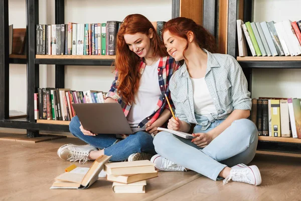 Dos Adolescentes Sonrientes Sentadas Piso Estantería Una Biblioteca Haciendo Deberes —  Fotos de Stock