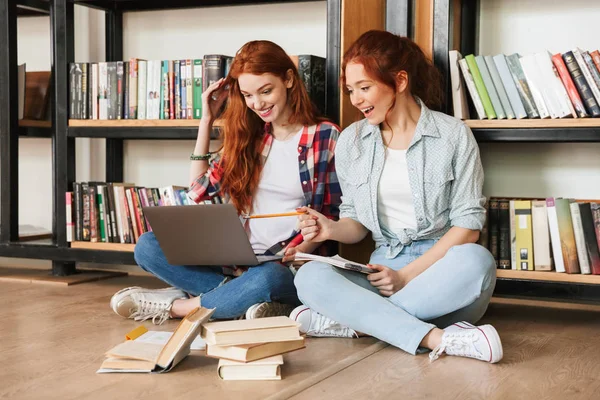 Dwa Szczęśliwy Nastoletnich Dziewcząt Siedząc Podłodze Półce Bibliotece Odrabiania Lekcji — Zdjęcie stockowe