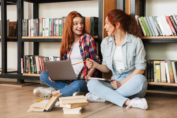 Dos Adolescentes Emocionadas Sentadas Piso Estantería Una Biblioteca Haciendo Deberes — Foto de Stock