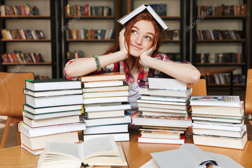 Smiling teenage girl sitting at the library table with big stacks of books